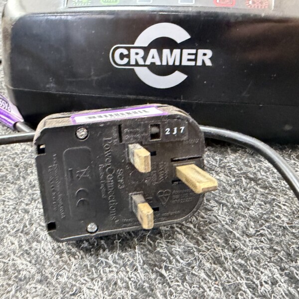 Close-up of a black CRAMER device with attached cables and a purple-labeled component on a textured surface.