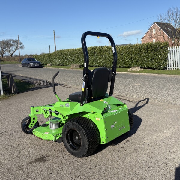 Bright green agricultural machine parked on a suburban street with a hedge and brick house in the background under a clear blue sky.