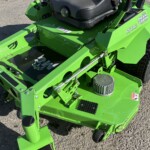 Bright green riding lawn mower frame with black seat, large rear tire, and metal bolts visible on pavement.