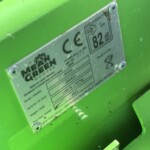 Close-up of a metal identification plate attached to a bright green lawn mower body, showing model and noise information.