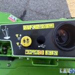 Close-up of a green machine control panel with yellow safety instruction stickers and a large circular opening to the right.