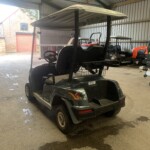 Indoor workshop with a black golf cart in the foreground and red utility tractors along the back wall behind a large open door.