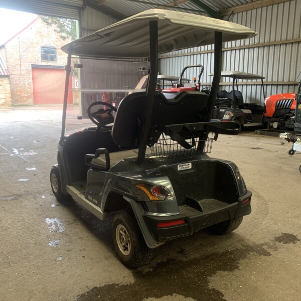 Indoor workshop with a black golf cart in the foreground and red utility tractors along the back wall behind a large open door.