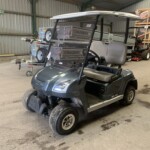 Grey golf cart with a white canopy inside a warehouse, carrying stacked Nugent metal equipment racks on its roof