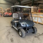 Blue golf cart with a white roof and the number 4 on its front, parked inside a storage warehouse with wooden crates and equipment nearby.