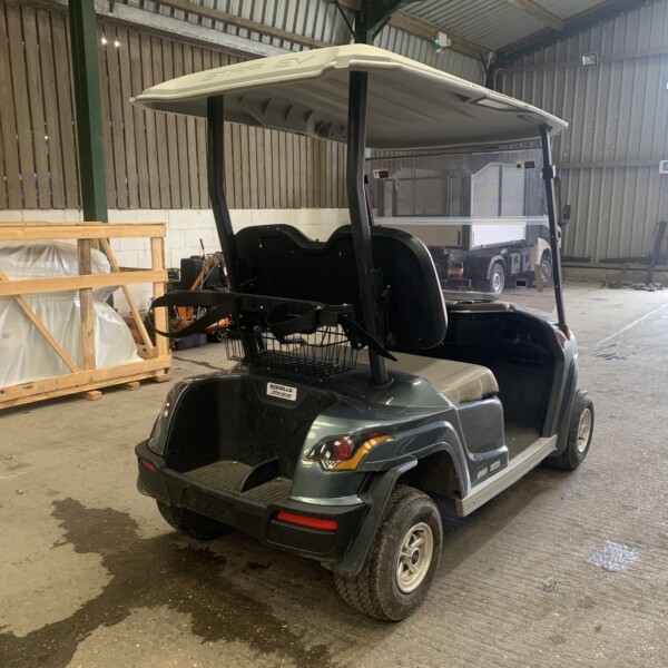 Electric golf cart with a white canopy parked inside a warehouse beside wooden crates and equipment to the left.