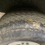 Close-up of a muddy tire tread with a penny for scale, inside a wheel well.