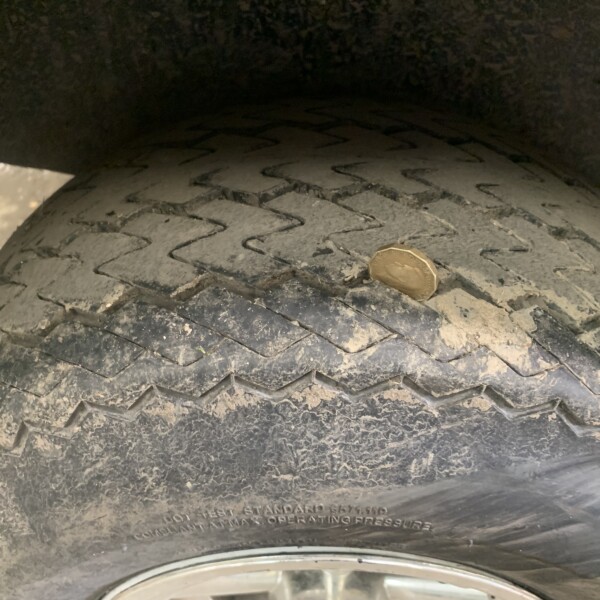 Close-up of a muddy tire tread with a penny for scale, inside a wheel well.