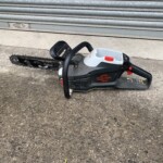 Gas-powered chainsaw resting on concrete near a closed, grey metal roll-up door.