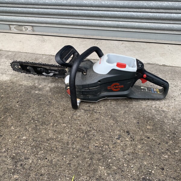 Gas-powered chainsaw resting on concrete near a closed, grey metal roll-up door.