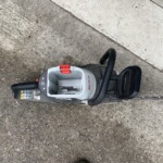 Electric power tool resting on rough pavement with a red latch and black handle, likely a portable saw or cutter on a construction site surface.