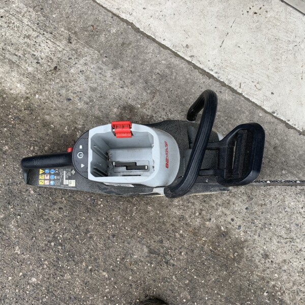 Electric power tool resting on rough pavement with a red latch and black handle, likely a portable saw or cutter on a construction site surface.