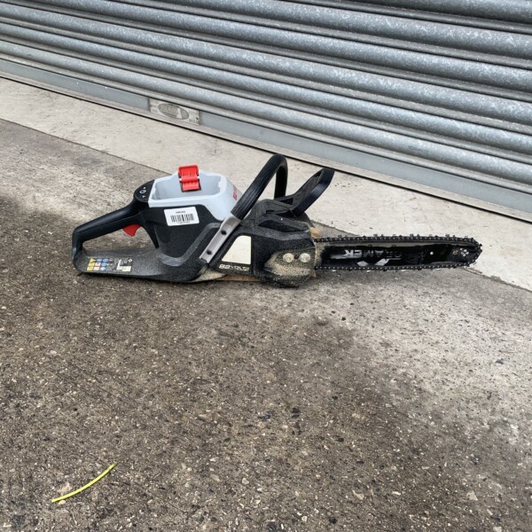 Cordless chainsaw lying on pavement in front of a gray metal roller shutter.