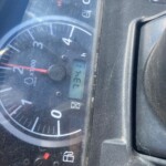 Close-up of a car instrument cluster with a circular tachometer and a red idle needle, plus a small digital mileage readout.