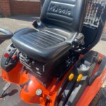 Black padded operator seat on an orange Kubota tractor, with control levers and pedals nearby.