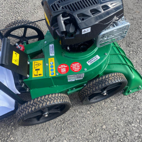 Green riding lawn mower with a black engine cover and large rear wheels on gravel.