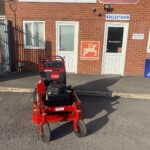 Red Toro ride-on lawn mower parked on asphalt outside a brick building with Russell's and TORO signs and a reception door.