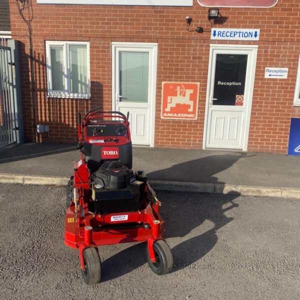 Red Toro ride-on lawn mower parked on asphalt outside a brick building with Russell's and TORO signs and a reception door.