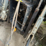 Close-up of muddy tractor attachment area with exposed gears, bolts, and metal frame components