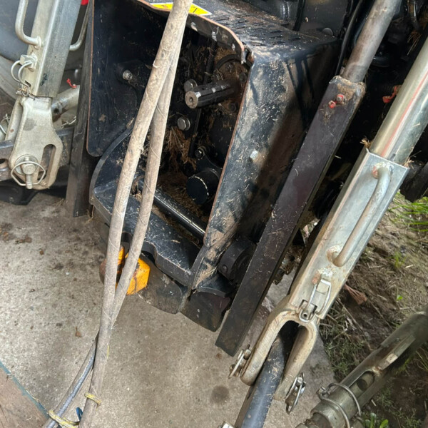 Close-up of muddy tractor attachment area with exposed gears, bolts, and metal frame components