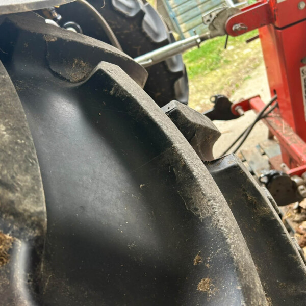 Close-up of a large, dirt-covered black tire with a red machinery frame visible in the background.