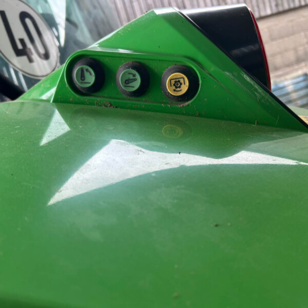 Close-up of a green mower dashboard with three round knobs and a yellow warning icon in the center-right area