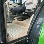 Inside the cab of a green tractor, showing the entry steps, foot pedals, and multiple control levers near the seat area
