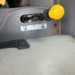 Close-up of a bright yellow rounded control lever on a gray vehicle dashboard, with a black boot and dusty interior visible in the slot.