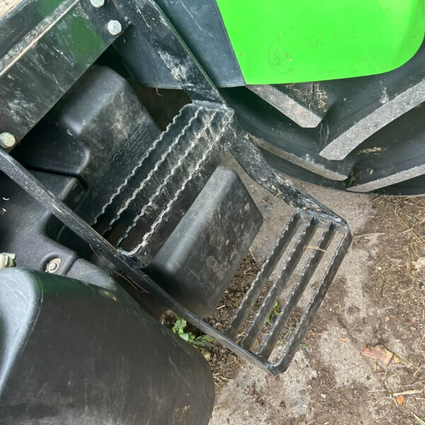 Close-up of a green agricultural machine showing its metal frame, bolts, and dirt on the track area.
