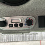 Close-up of a car climate control panel showing a temperature dial with blue/red indicator and a fan control on a silver console, set against a gray dashboard.