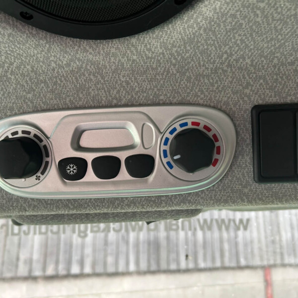 Close-up of a car climate control panel showing a temperature dial with blue/red indicator and a fan control on a silver console, set against a gray dashboard.