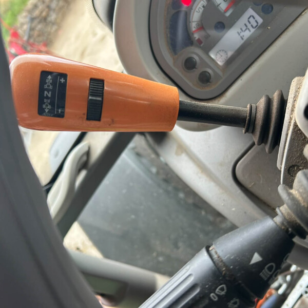 Close-up of an orange control lever with a black adjustment knob, mounted inside a machine, with a dial/gauge in the background.