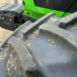 Close-up of a dirty black excavator bucket with dirt on the teeth and a green construction machine in the background