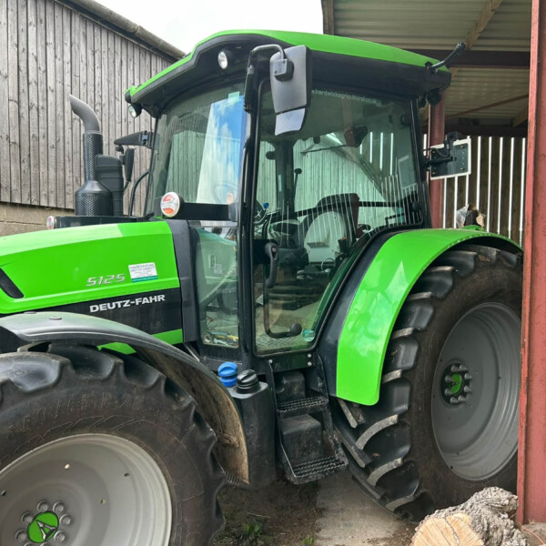 Front of a green Deutz-Fahr 5125 tractor parked in a shed with wooden walls and red support beam, visible cab and large tires.