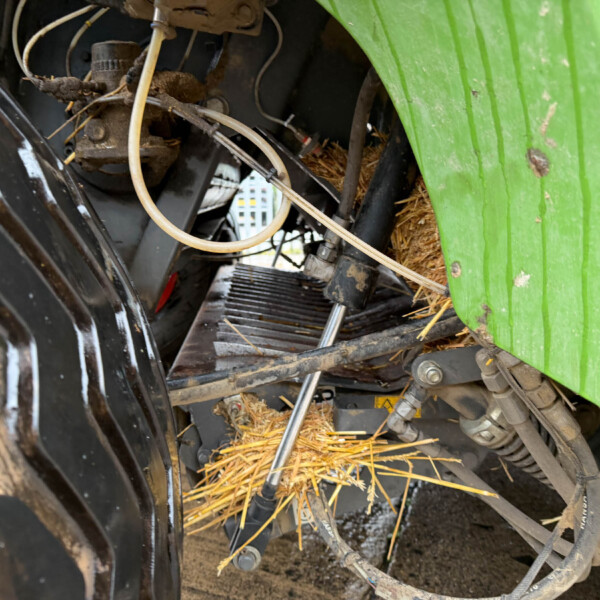 Close-up of tangled hoses, wires, and metal framework inside a green agricultural machine, with straw and dirt visible around the components