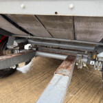 Underside view of a heavy-duty trailer with metal beams, hydraulic cylinders, and a tire with a red rim.