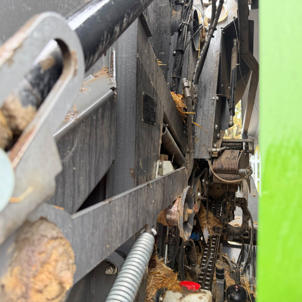 Close-up view inside industrial equipment showing belts, hoses, and metal components with wood debris and a bright green panel on the right side.