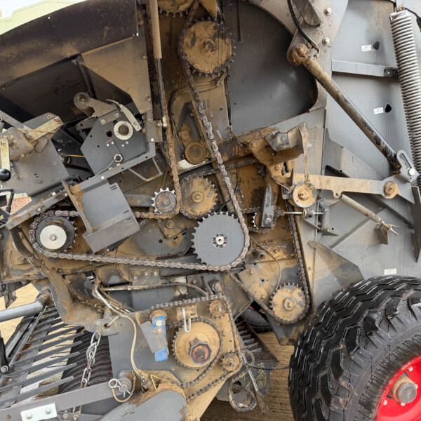 Exposed gears, chains, and belts of a dusty agricultural harvester mechanism with large tires nearby