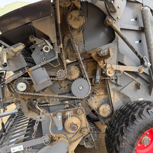 Close-up of a muddy industrial machine's gears, chains, and belts with a large tire in the foreground.