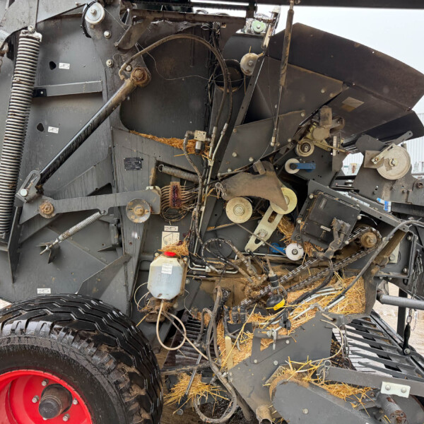 Close-up of a large gray farming harvester's internal mechanism with belts, hoses, and a bright red wheel.