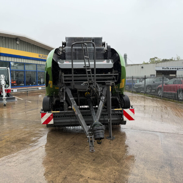 Front view of a large green agricultural harvester on a wet showroom lot, with New Holland Agriculture signage and a Volkswagen building in the background.