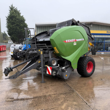 Green Fendt agricultural header on a trailer in a wet dealership yard with a Russells building in the background