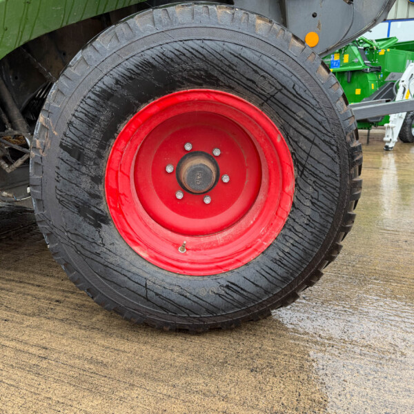 Close-up of a large tractor tire with a red rim in a workshop setting, wet ground visible.