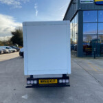 Rear view of a large white trailer in a parking lot beside a modern glass-front building, license plate WR59 KUT