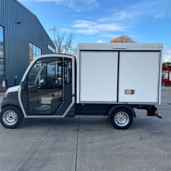 White panel delivery truck with a large enclosed cargo box parked beside a modern industrial building under a blue sky