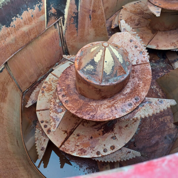 Close-up of rusted circular gears and plates with jagged teeth inside a weathered industrial chamber.