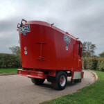 Red tanker trailer parked on a curved road under a cloudy sky, with hedges and trees in the background.