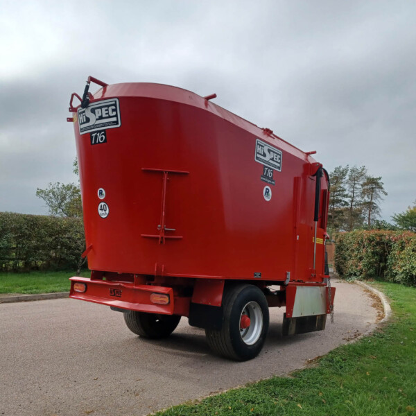 Red tanker trailer parked on a curved road under a cloudy sky, with hedges and trees in the background.