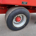 Close-up of a large truck tire mounted on a red trailer, with a sticker that reads 'Check tightness of nuts and tyre pressure' above it