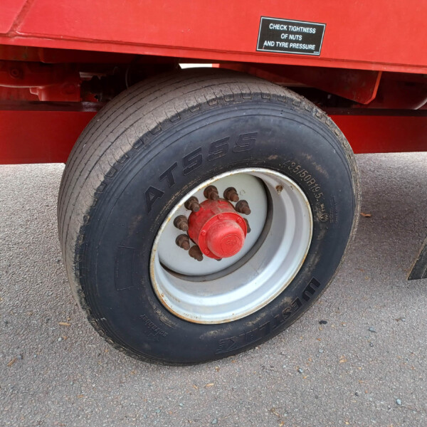 Close-up of a large truck tire mounted on a red trailer, with a sticker that reads 'Check tightness of nuts and tyre pressure' above it